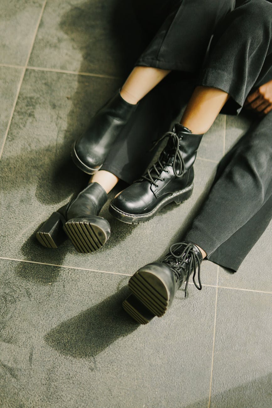legs in black shoes and pants of two unrecognizable persons sitting on floor