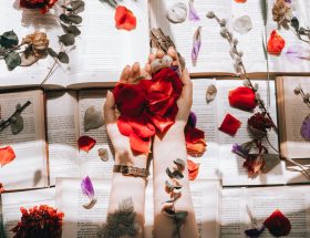 crop woman with bright flower petals on books