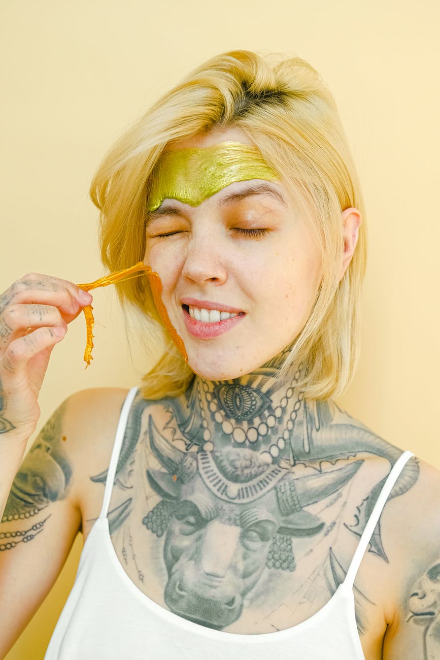 young tattooed woman pulling off facial mask