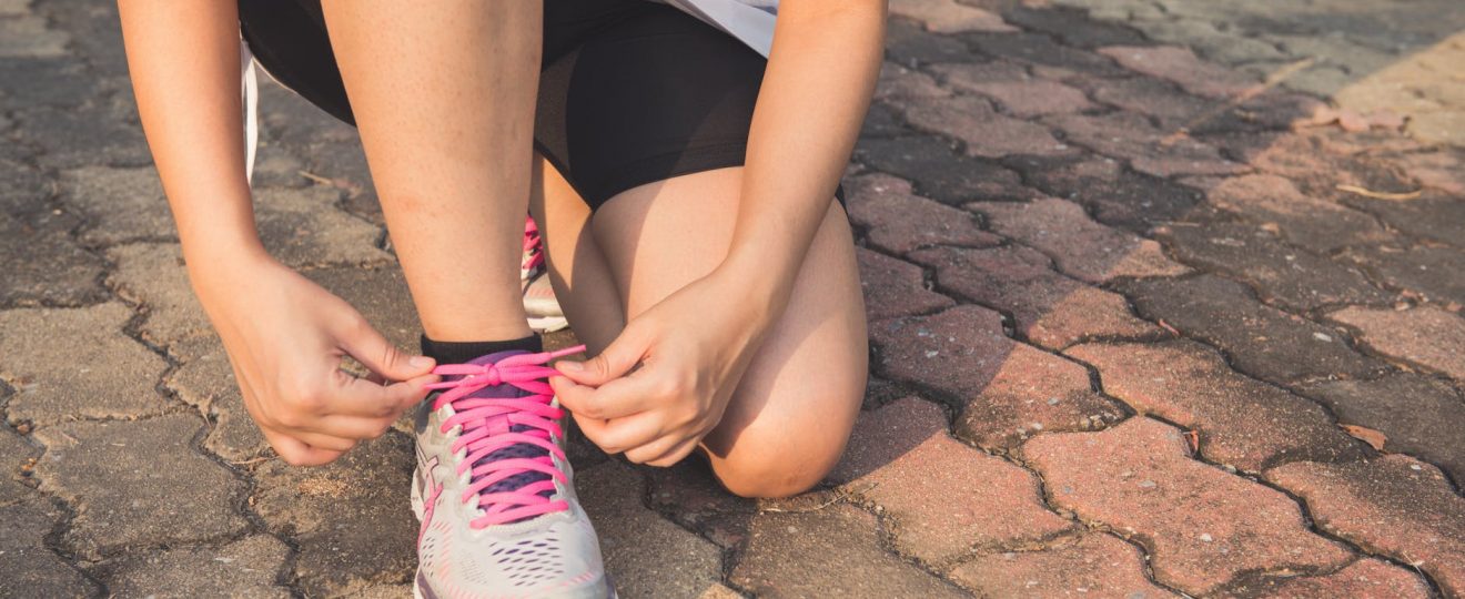 woman lacing up her gray and pink nike low top athletic shoe