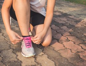 woman lacing up her gray and pink nike low top athletic shoe