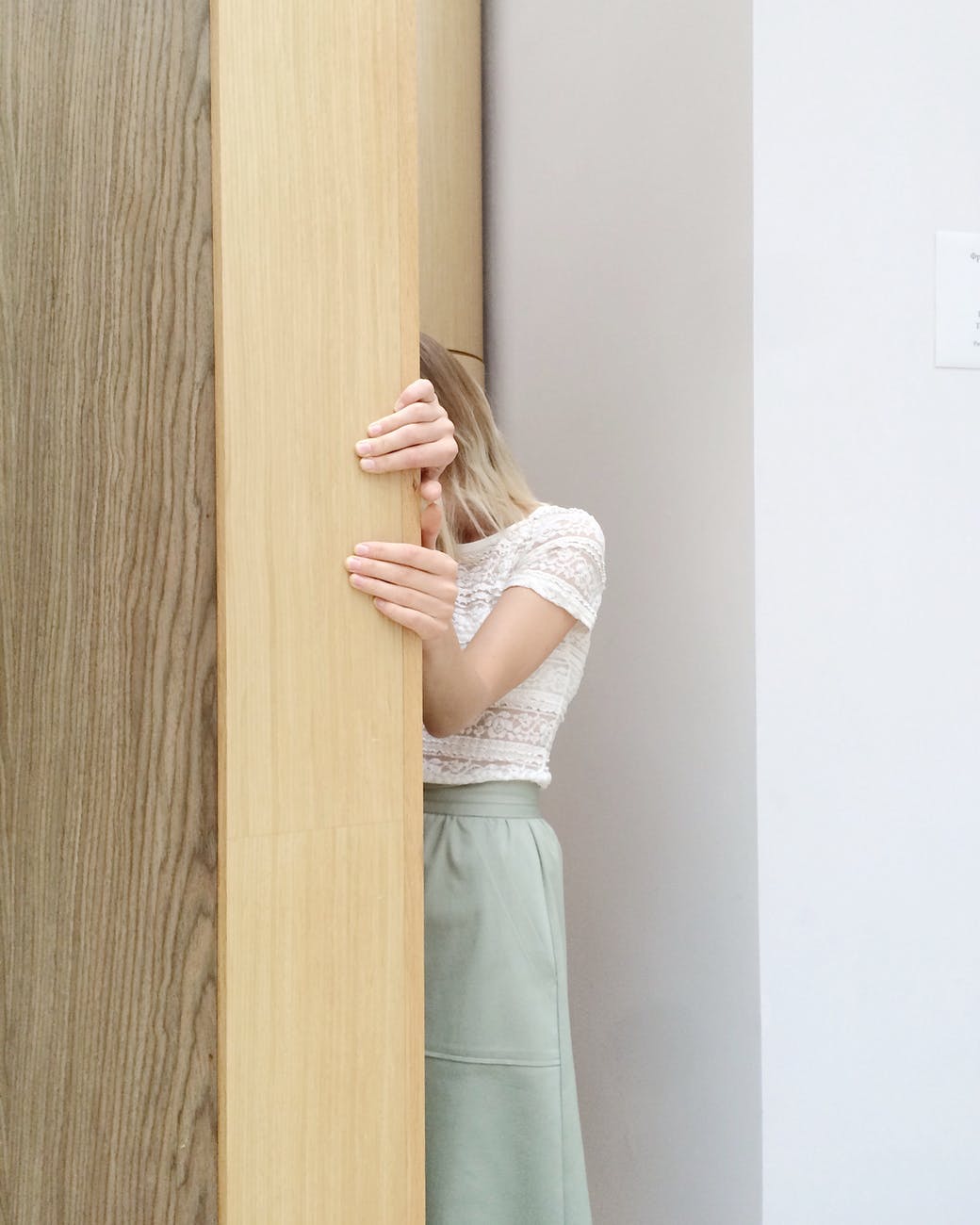 woman in white lace cap sleeved top and green skirt hiding behind brown wall