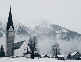 bird's-eye view photography of houses and cathedral near snow mountain