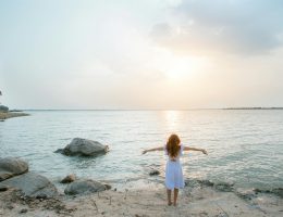 woman in white shirt standing on gray rock near body of water